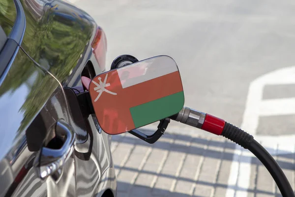 Flag of Oman on the car\'s fuel tank filler flap. Fueling car with petrol pump at a gas station. Petrol station. Gasoline and oil products. Close up.