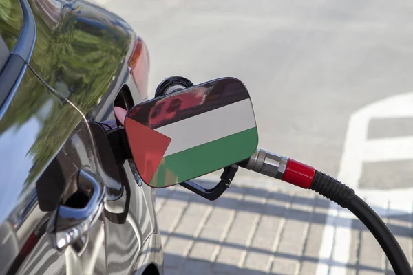 Flag of Palestine on the car\'s fuel tank filler flap. Fueling car with petrol pump at a gas station. Petrol station. Gasoline and oil products. Close up.