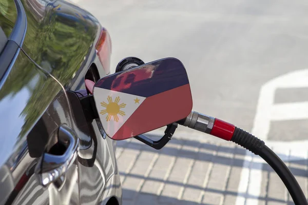 Flag of Philippines on the car\'s fuel tank filler flap. Fueling car with petrol pump at a gas station. Petrol station. Gasoline and oil products. Close up.