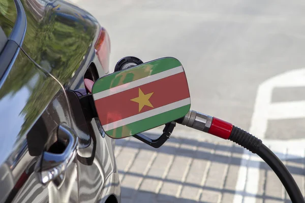 Flag of Suriname on the car\'s fuel tank filler flap. Fueling car with petrol pump at a gas station. Petrol station. Gasoline and oil products. Close up.