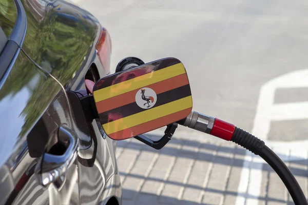 Flag of Uganda on the car\'s fuel tank filler flap. Fueling car with petrol pump at a gas station. Petrol station. Gasoline and oil products. Close up.