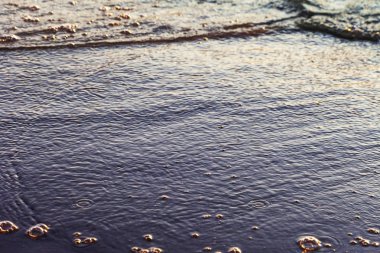 Dalgalar büyük bir nehir kıyısında kumlu. Işık ışınları dalgalar halinde yansıtılır,