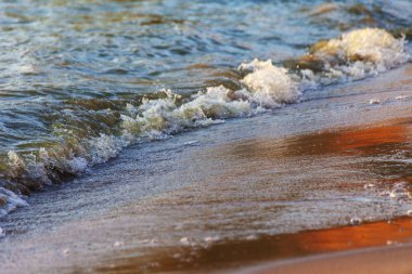 Dalgalar büyük bir nehir kıyısında kumlu. Işık ışınları dalgalar halinde yansıtılır,