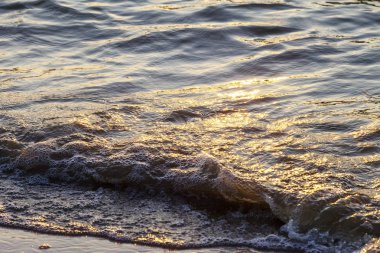 Dalgalar büyük bir nehir kıyısında kumlu. Işık ışınları dalgalar halinde yansıtılır,