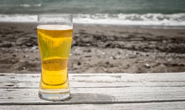 Karanlık kum ve kırma sörf içinde belgili tanımlık geçmiş ile deniz kenarında kum rustik bir masada açık havada üzerinde ışık altın Pilsner gazoz