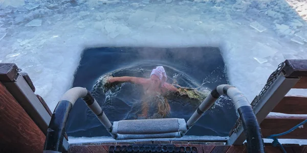 在从出口梯子顶部看的河或湖的冰水中游泳后的人在冰洞中堆起 — 图库照片