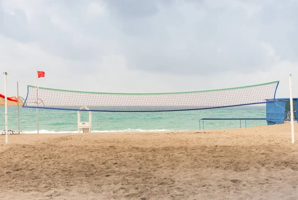 Volley ball net on a deserted tropical beach with footprints in the sand and a calm ocean under a cloudy sky