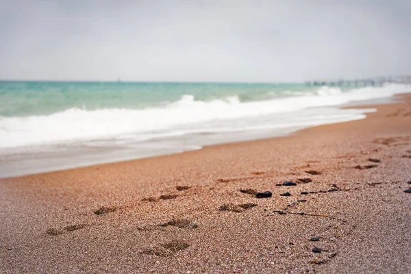 波が海岸と灰色の雲に覆われた空側ビネット嵐ビーチの砂の上の足跡 — ストック写真