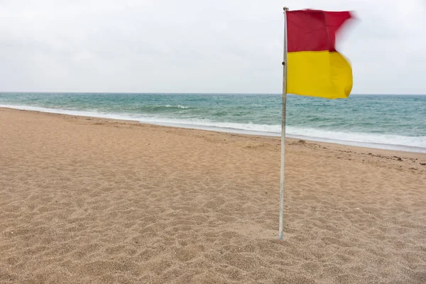 灰色の空の日が途切れ海と無人島の砂浜のビーチで風になびいて赤と黄色の警告フラグ — ストック写真