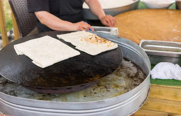 stock image Man cooking Gozleme flatbread, a traditional Anatolian savory snack, on a griddle to crisp it after brushing it with egg and butter