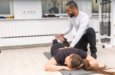 Erkek eğitmen buzağı genç kadının spor salonunda yalan germe.