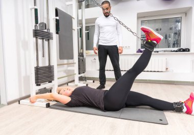 Genç kadın eğitim ayak vasıl jimnastik salonu mat yatarken kablo crossover makine üzerinde