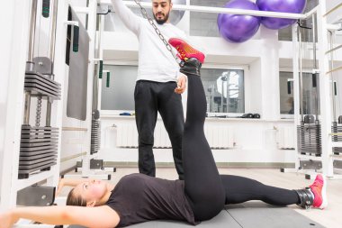 Spor salonunda kadın egzersiz bacak kablo crossover makinede eğitmen ile yardımcı