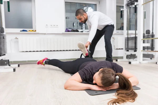 私人教练协助妇女在健身房锻炼腿部 — 图库照片