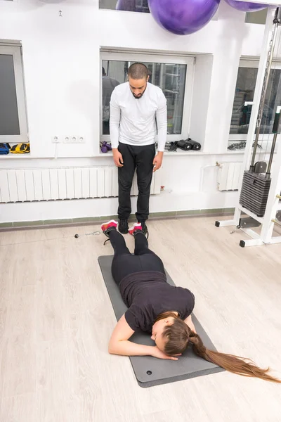 Kadın spor salonunda eğitmenle egzersiz yapıyor.