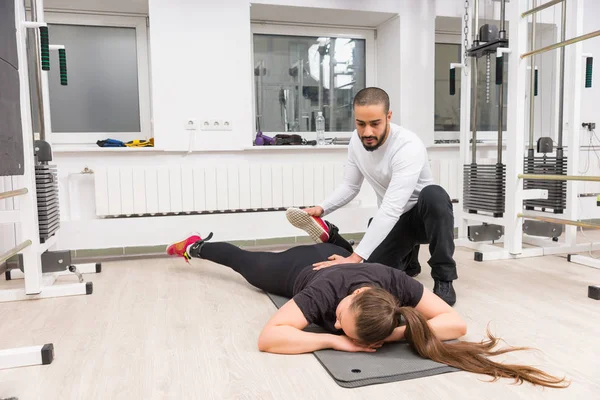 Sağlık ve fitness kavramı bir mat üzerinde yalan söylüyor gibi bacağını geri bükme bir spor salonunda bir kadın onun egzersiz ile yardımcı antrenör