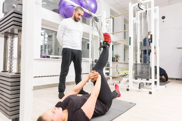 个人教练看妇女在健身房有线交叉机上锻炼 — 图库照片