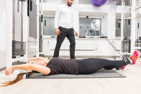 Woman exercising legs on cable machine while lying on mat at gym