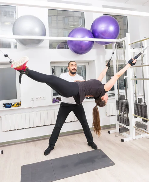 Fit woman exercising with suspension straps under the supervision of a professional fitness instructor at the gym
