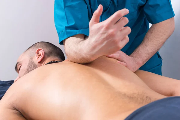 Professional masseur doing a spine massage on a male client applying pressure along the vertebrae with his forearm in a close up cropped view