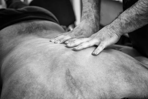 Black and White Close Up Detail of Male Massage Therapist Hands Giving Back Rub Down to Unidentifiable Male Client Lying on Stomach