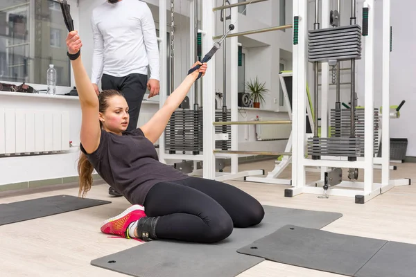 Spor salonunda egzersiz yaparken kablo crossover makine kullanan genç kadın