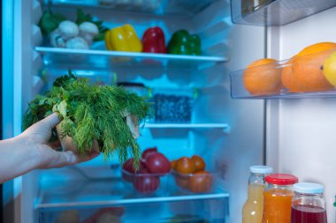 Taze dereotu sepetle karşı açık buzdolabı tutan kişi