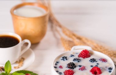 Süt ve ahududu, yaban mersini ve bir fincan sade kahve servis böğürtlen gibi meyveleri ile tepesinde kahvaltılık gevrek kase