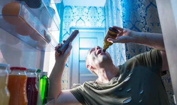 Человек Вытаскивает Бутылку Пива Холодильника Держа Другой Руке Целую Салями — стоковое фото