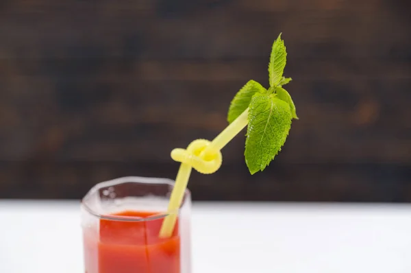 Glass of fresh tomato juice with straw and mint leaf in close up view