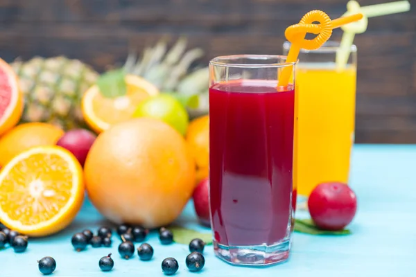 Two glasses of freshly squeezed juice with assorted tropical fruit and berries on a blue table in a healthy diet concept