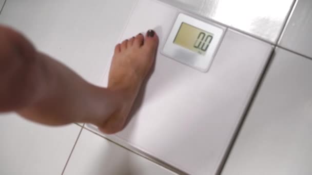 Женщина наступает на весы в ванной — стоковое видео
