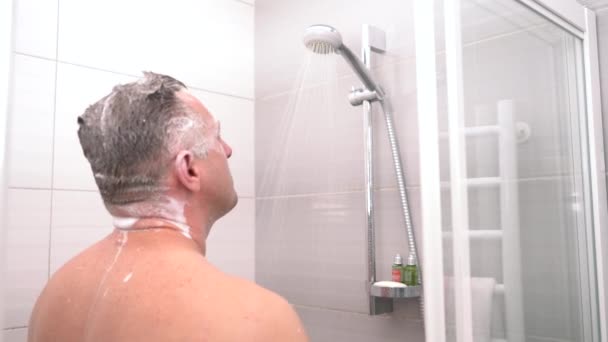 Middle-aged man shampooing his hair in a shower — Stockvideo