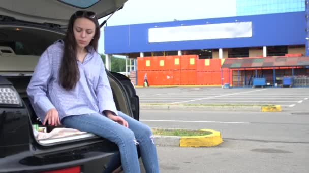 Mujer joven sentada en el maletero de un coche comiendo — Vídeo de stock