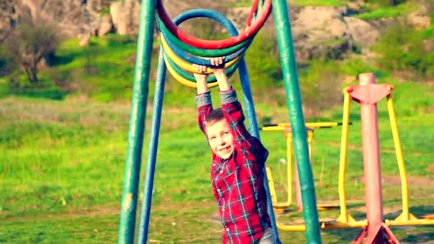 小男孩在公园或乡下的孩子操场上玩着五颜六色的圆形酒吧的秋千 — 图库视频影像