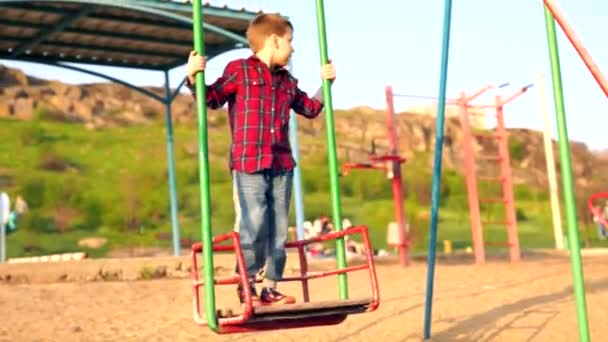 Kleiner Junge Jeans Spielt Auf Einer Schaukel Auf Einem Sandigen — Stockvideo