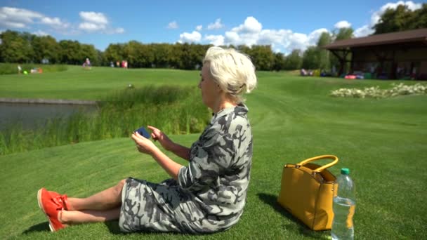 Зріла жінка сидить на зеленій траві — стокове відео