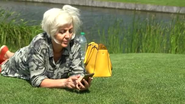 Middle-aged woman relaxing on grass beside a lake — Stock Video