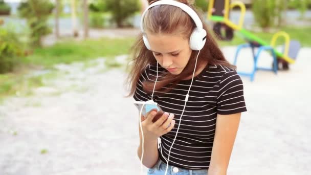 Flickan bär hörlurar medan du håller telefonen — Stockvideo