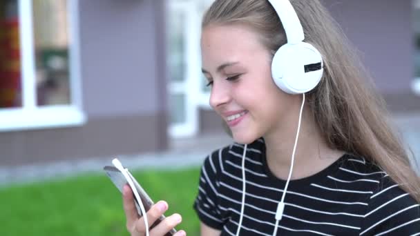 Teen s sluchátka se usmívá na chytrý telefon — Stock video