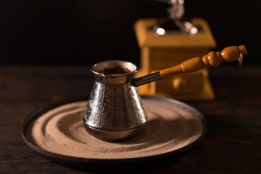 Küçük kazınmış metal pot bulanık açık renkli ahşap kahve değirmeni önünde dekoratif ahşap saplı