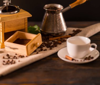 Bir kahve değirmeni ile taze çekilmiş kahve ile birlikte bir beyaz Kupası ve cezve rustik bir mutfak bir kumaş üzerine açık çekmece