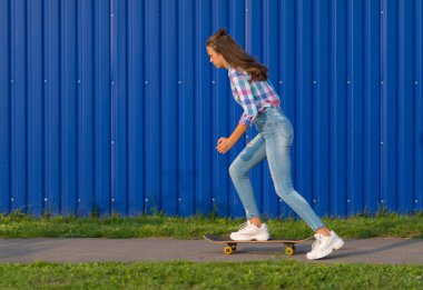 Uzun kahverengi saçlı mavi duvar önünde kentsel bir yol boyunca alacakaranlıkta kaykay trendy ince genç kadın