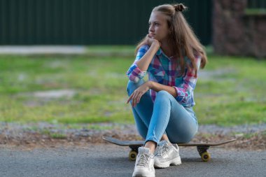 Oturan sıkılmış genç kadın çenesinin elinde dinlenme ile gelmesi için birini izlerken bir kaykay üzerinde bekleyen ve alanı kopyalayın