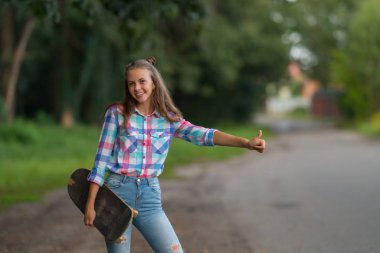 Mutlu çekici genç öğrenci gibi o kolunu kameraya gülümseyen altında duran bir kaykay olan yol kenarındaki bir Asansör karıştırıyorum