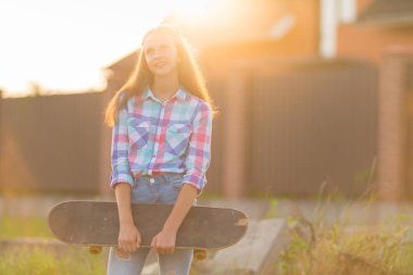 Genç kız onun kaykay içinde yüksek bir anahtar portre tutan bir kentsel evin önünde günbatımı sıcak kızdırma ayakta