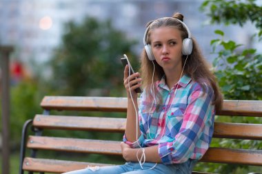Onun mobile ile stereo kulaklık müzik dinlemek bir parkta bankta oturur gibi onun dudakları pursing düşünceli genç kadın