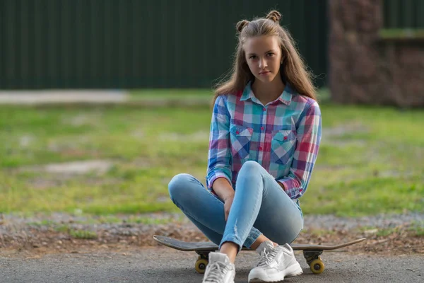 彼女は コピー領域とビューを間近に彼女のスケート ボードに道路の側で待っている座っているとカメラを厳粛に見つめ思いやりのある若い女性 — ストック写真
