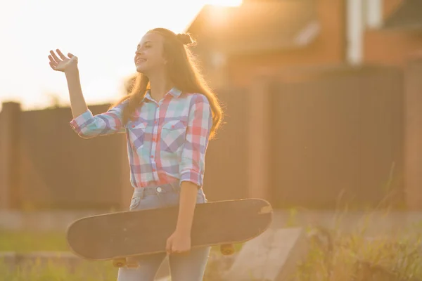笑顔の女性 代のジーンズを着て スケート ボードを押しながらオレンジ レンズ フレアを引き起こす太陽の光によって照らされています — ストック写真