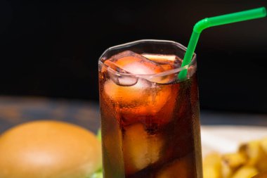 Buz küçük buz küpleri ve yeşil saman hamburger ve patates kızartması arka planda otururken içinde sıkışmış soda camına yakın çekim